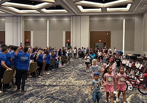 A group of children entereing the room where they are receiving their donated bike made during the wheels for the world team building event
